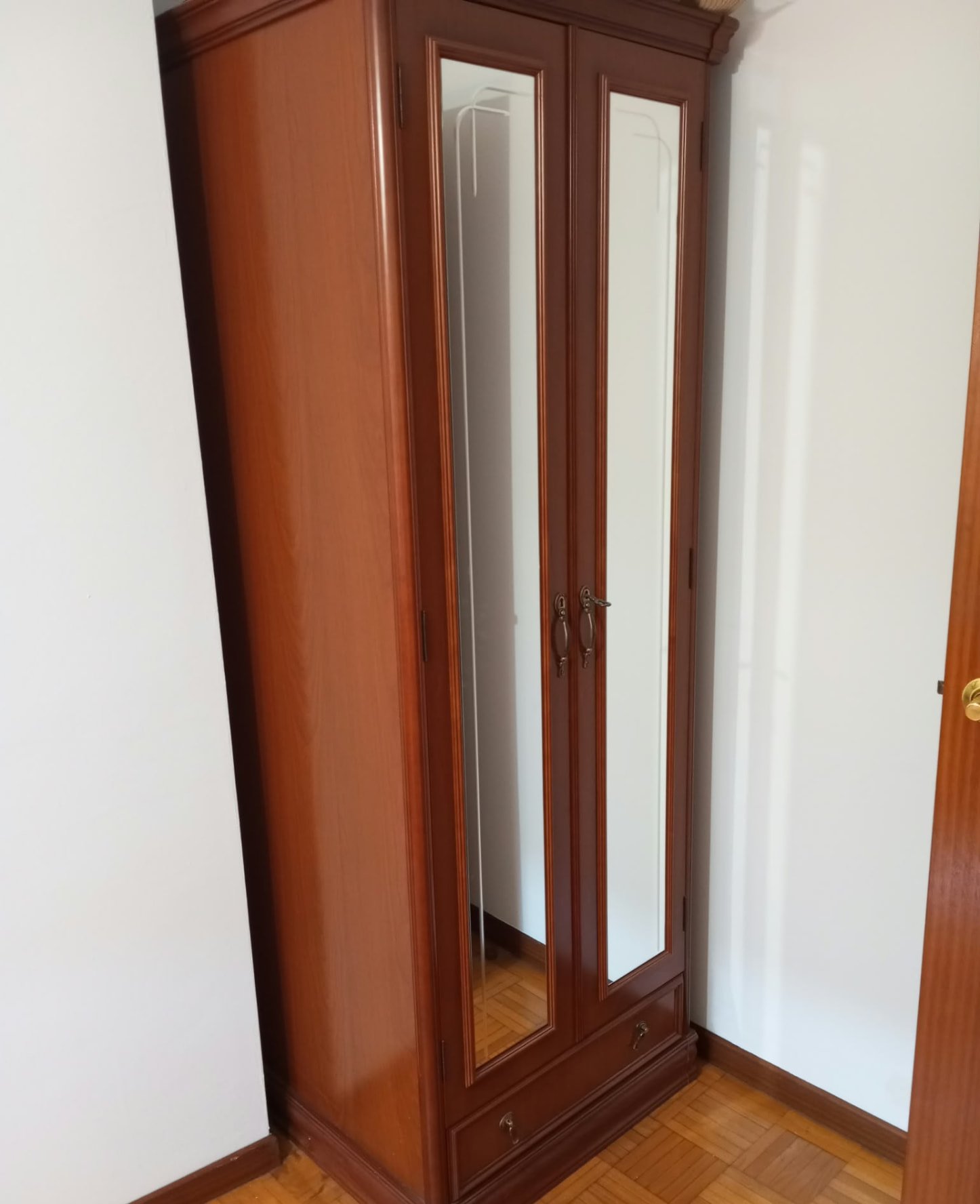 Rincón de dormitorio con paredes blancas y armario de madera con espejos