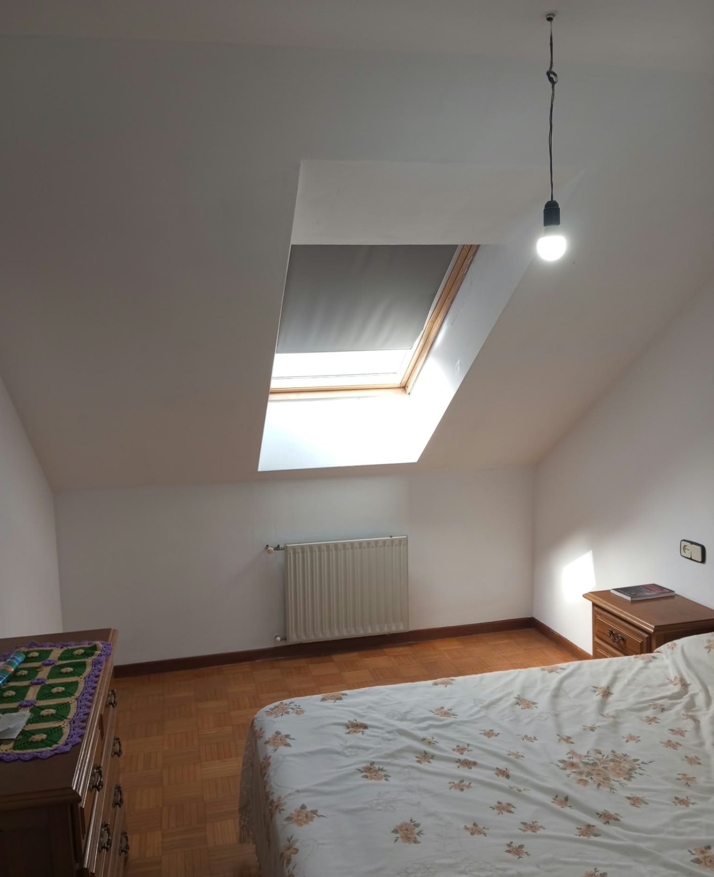 Dormitorio abuhardillado con techo y paredes pintados en blanco junto a ventana de tejado