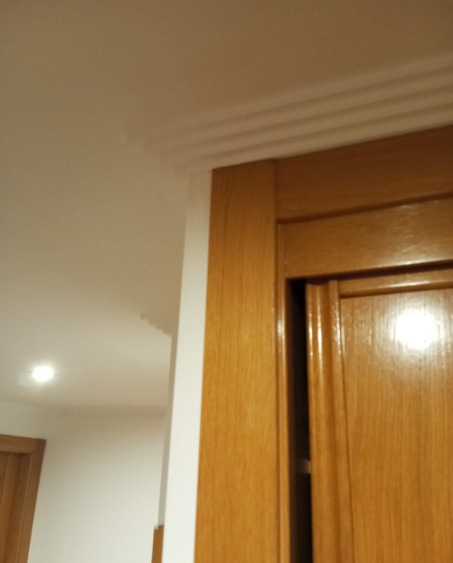 Moldura de techo pintada en blanco junto a puerta de madera barnizada