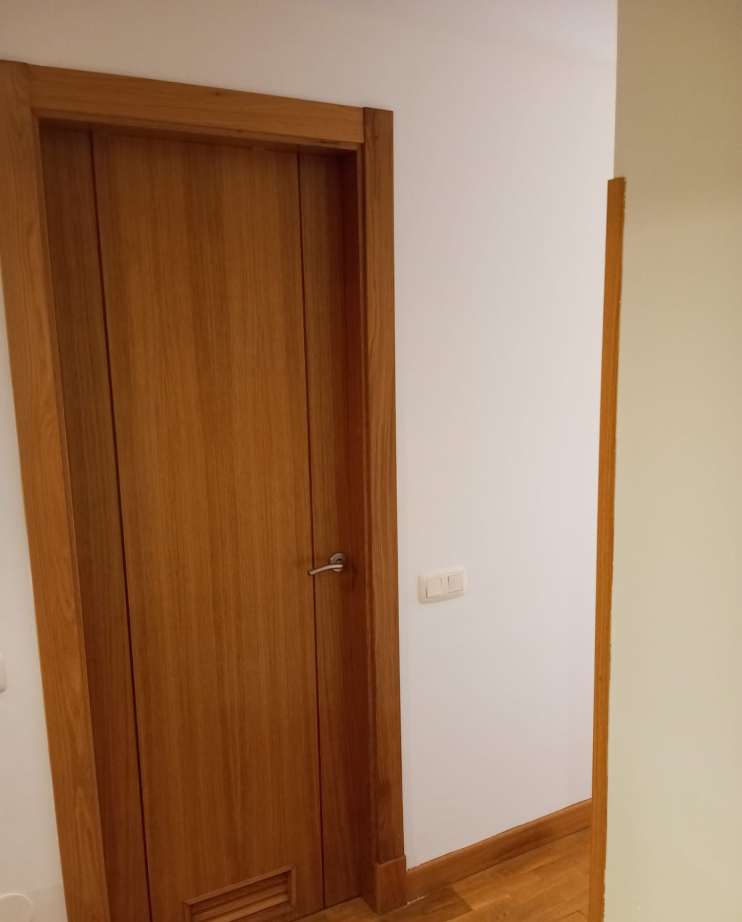 Puerta de madera barnizada junto a pared pintada en blanco