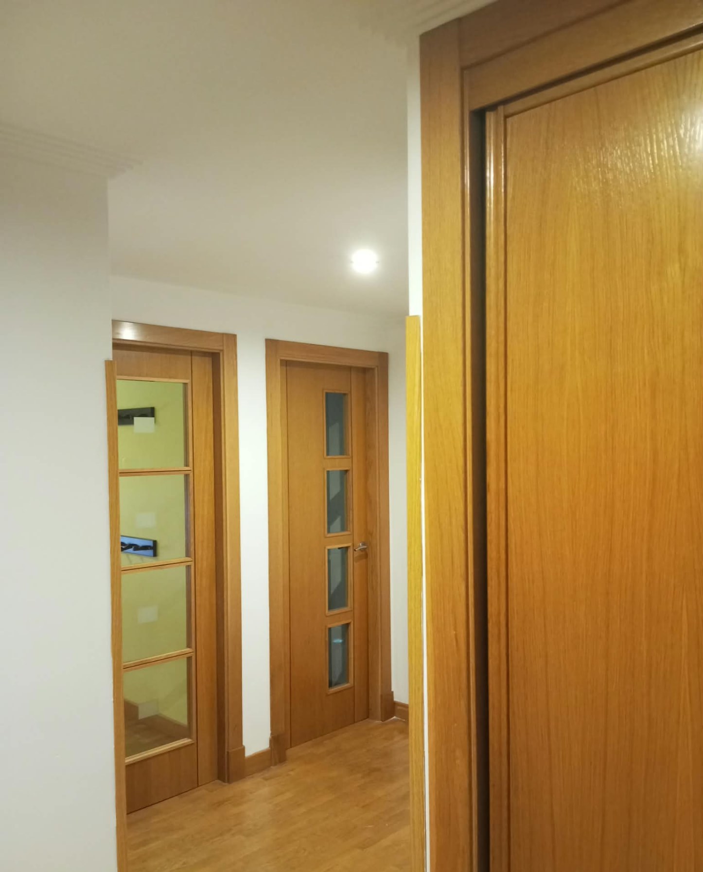 Pasillo con varias puertas de madera barnizada y paredes blancas