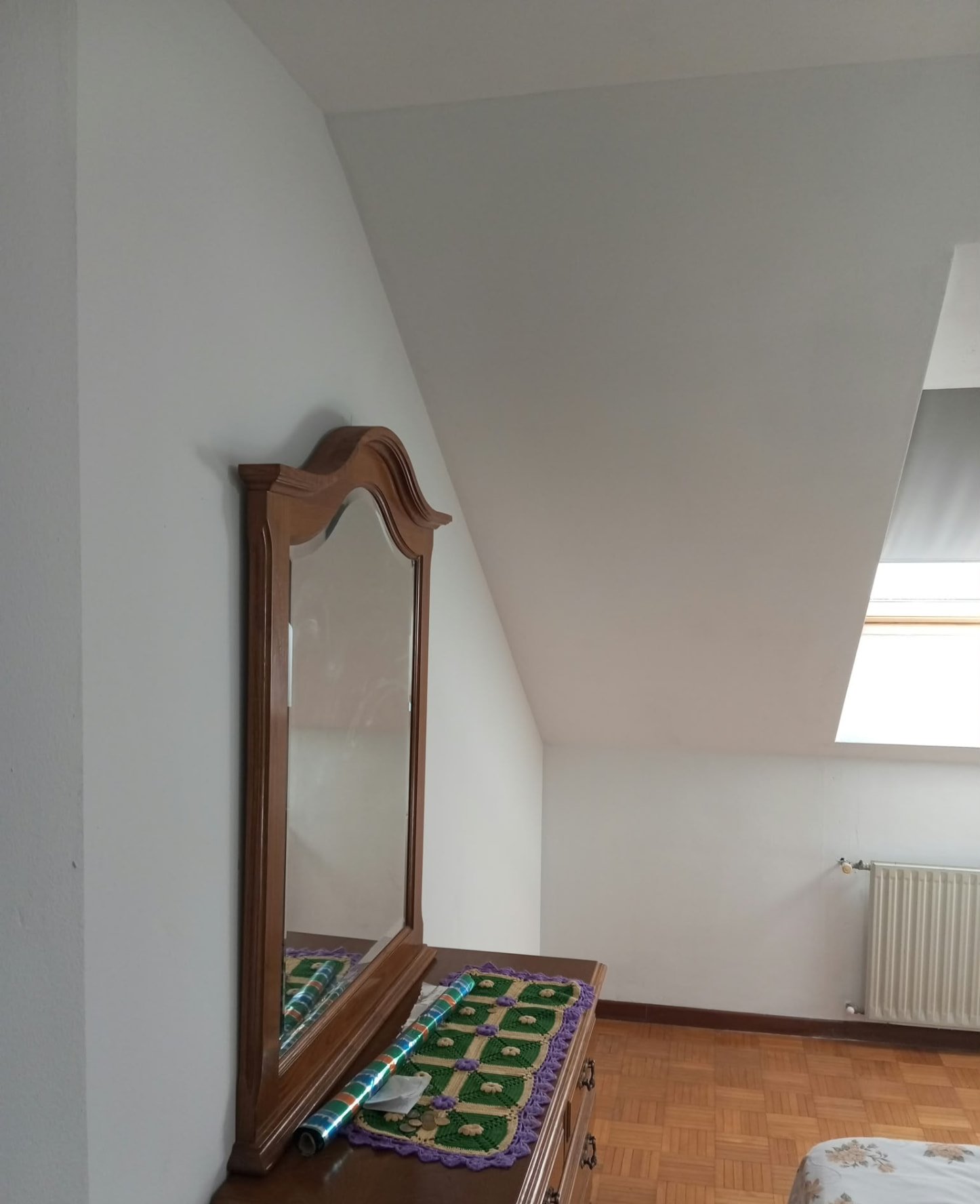 Dormitorio abuhardillado pintado en blanco con cómoda y ventana de tejado