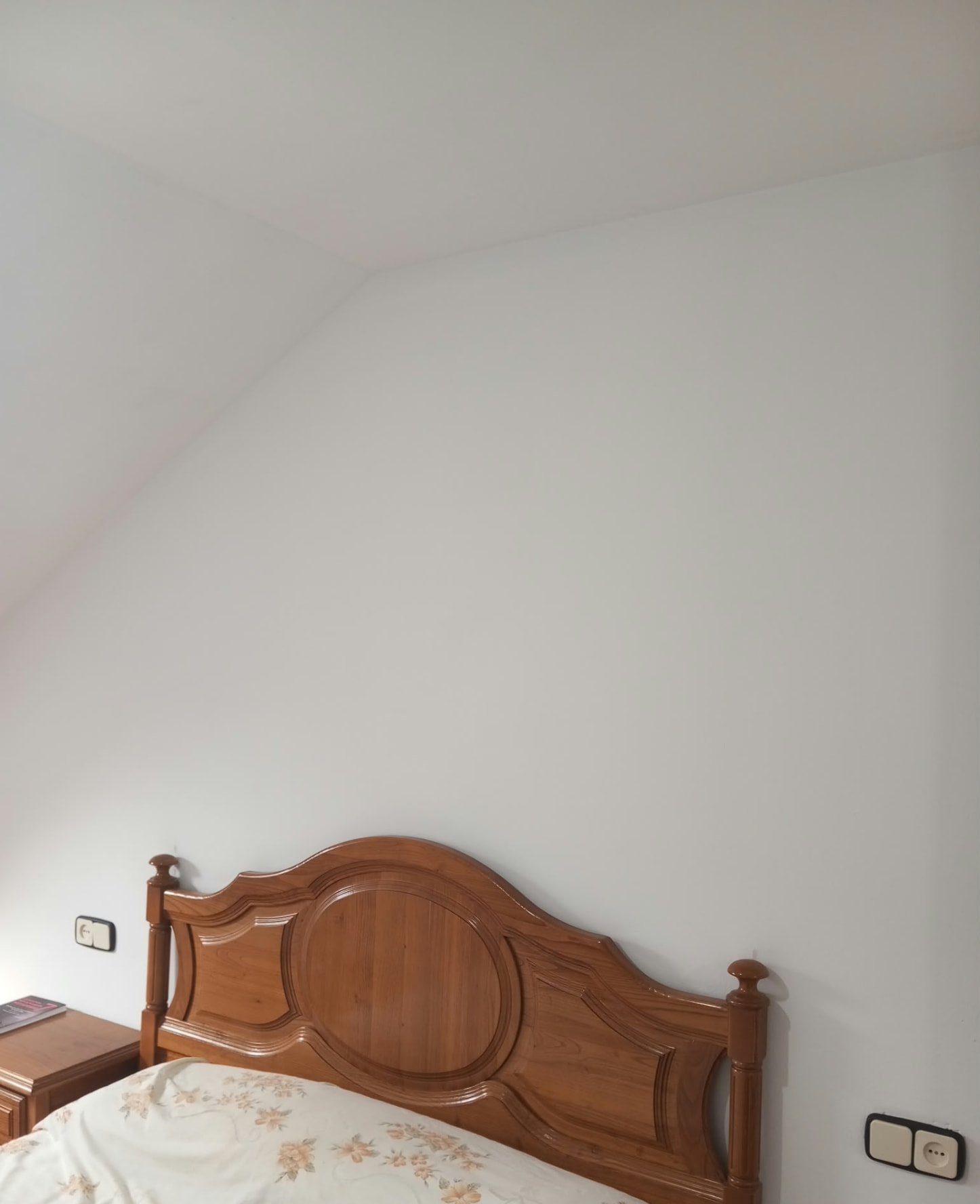 Pared de dormitorio abuhardillado pintada en blanco sobre cabecero de madera