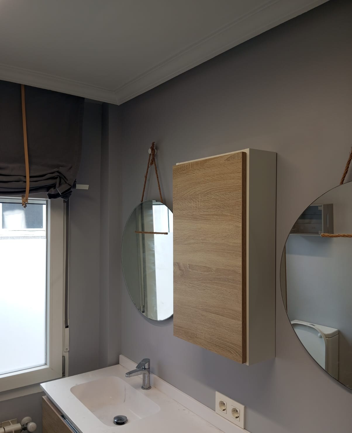 Baño con paredes grises, moldura blanca y espejos redondos