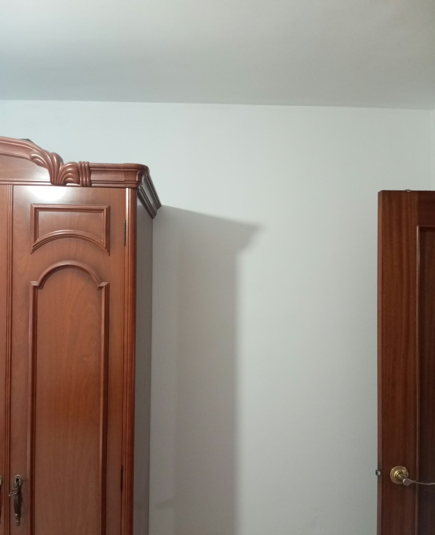 Pared de dormitorio pintada en blanco entre armario y puerta de madera