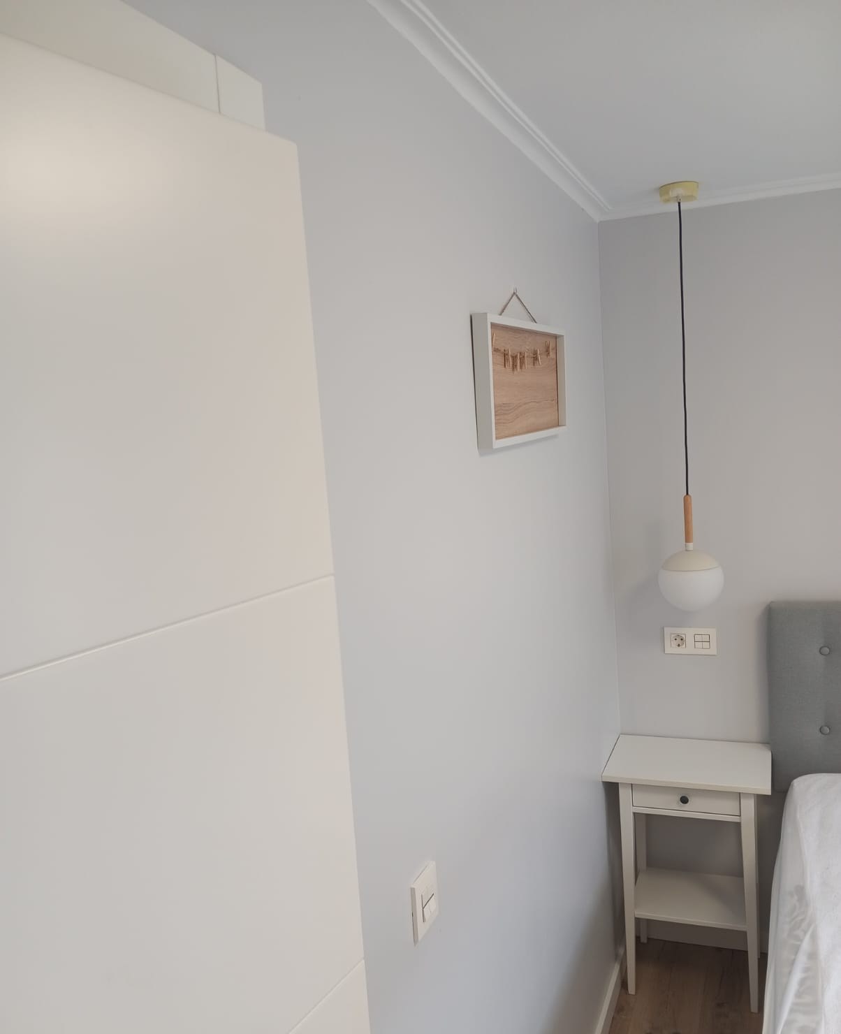 Pared de dormitorio pintada en gris claro con lámpara colgante