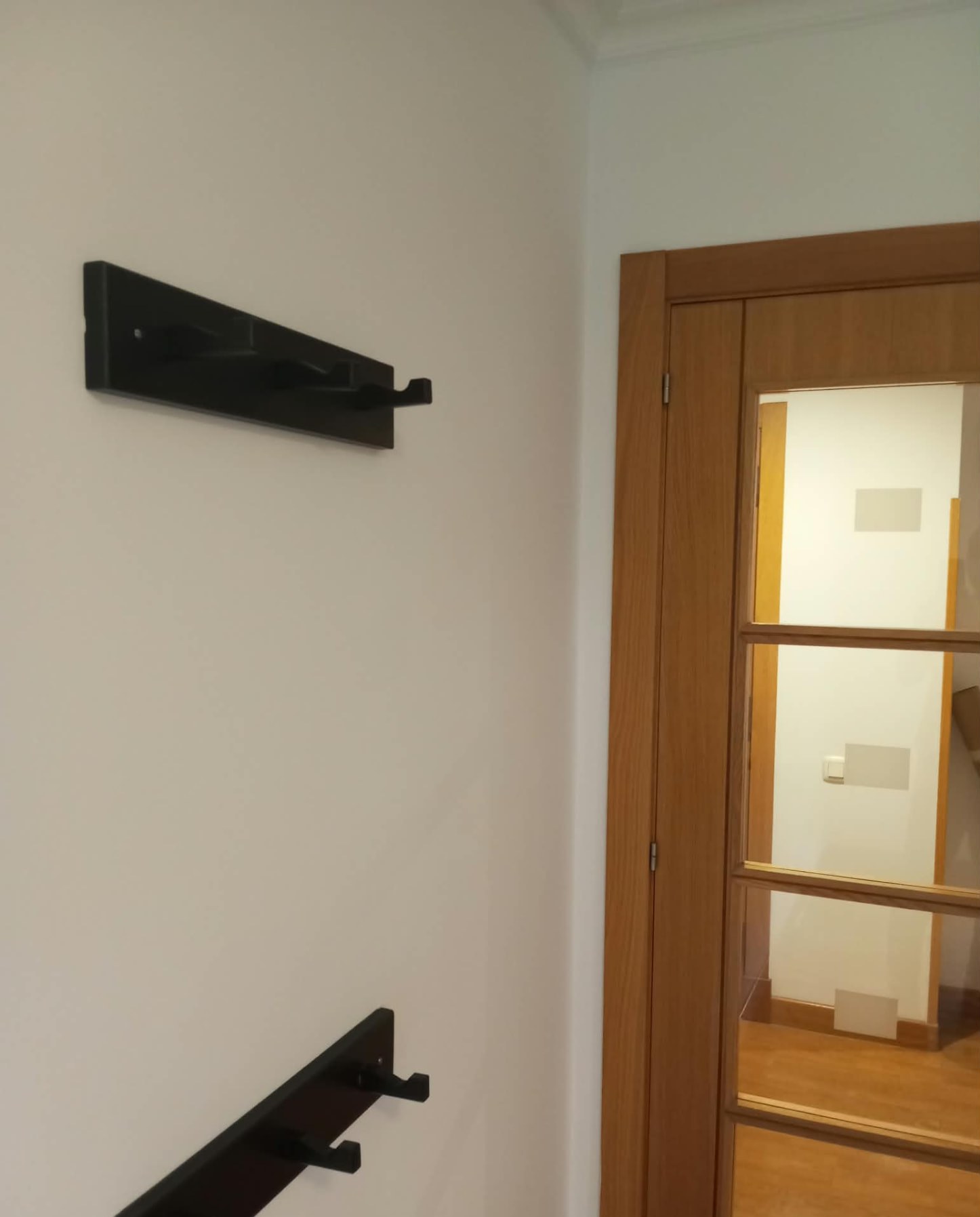 Pared pintada en blanco con percheros junto a puerta de madera