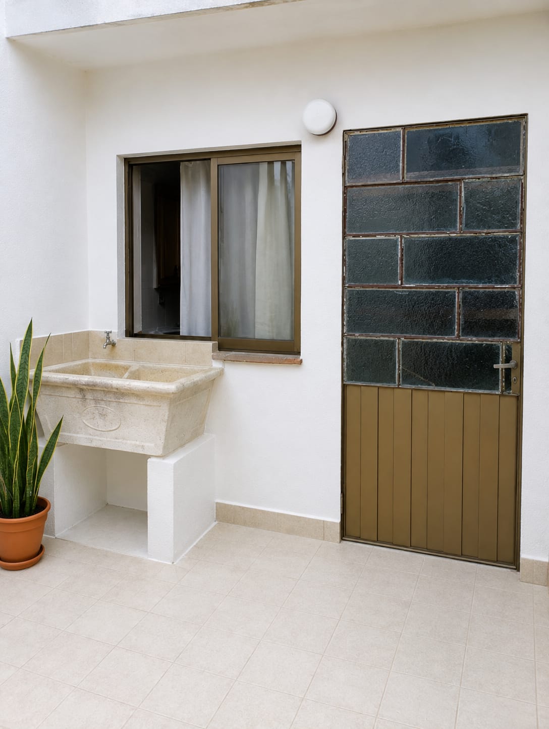 Patio exterior con paredes pintadas en blanco, pila de lavar y puerta barnizada