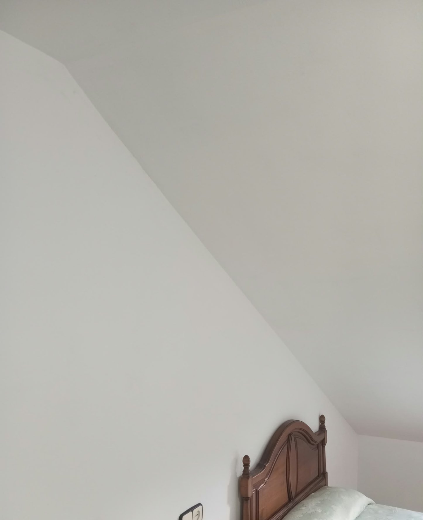 Pared inclinada de dormitorio pintada en blanco sobre cabecero de madera