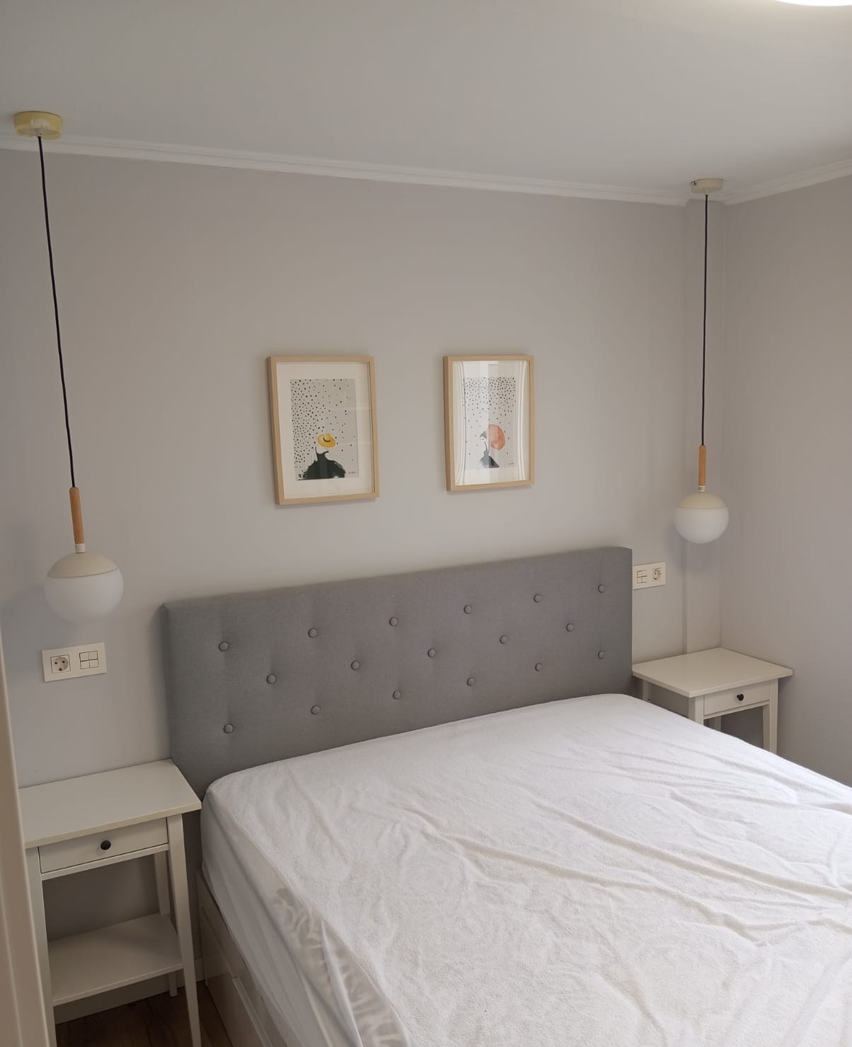 Dormitorio pintado en gris claro con cabecero tapizado y lámparas colgantes