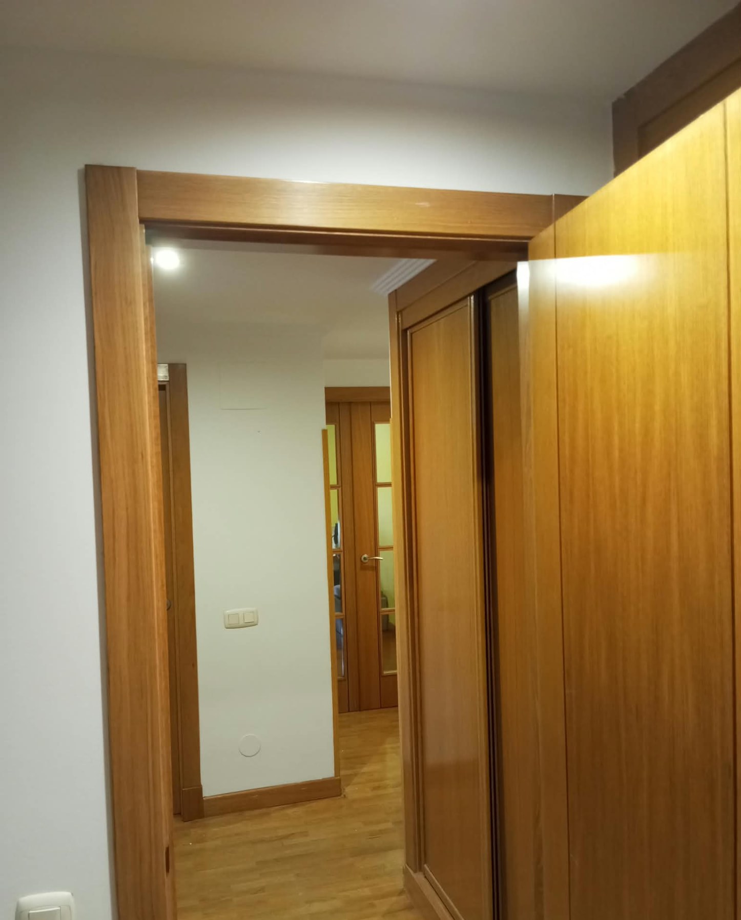 Pasillo con armarios correderos de madera barnizada y paredes pintadas en blanco