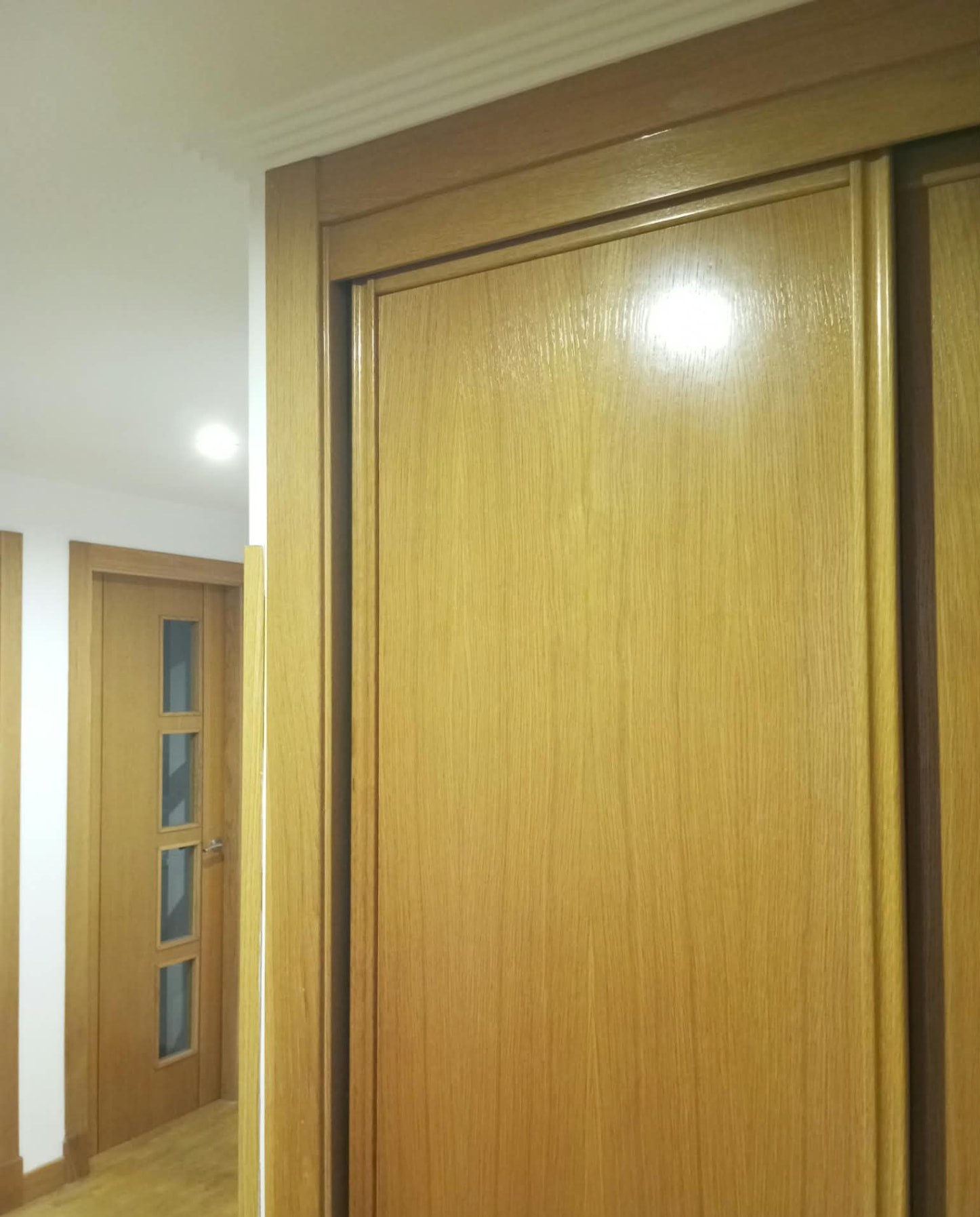 Detalle de puerta de madera barnizada con brillo junto a pasillo pintado