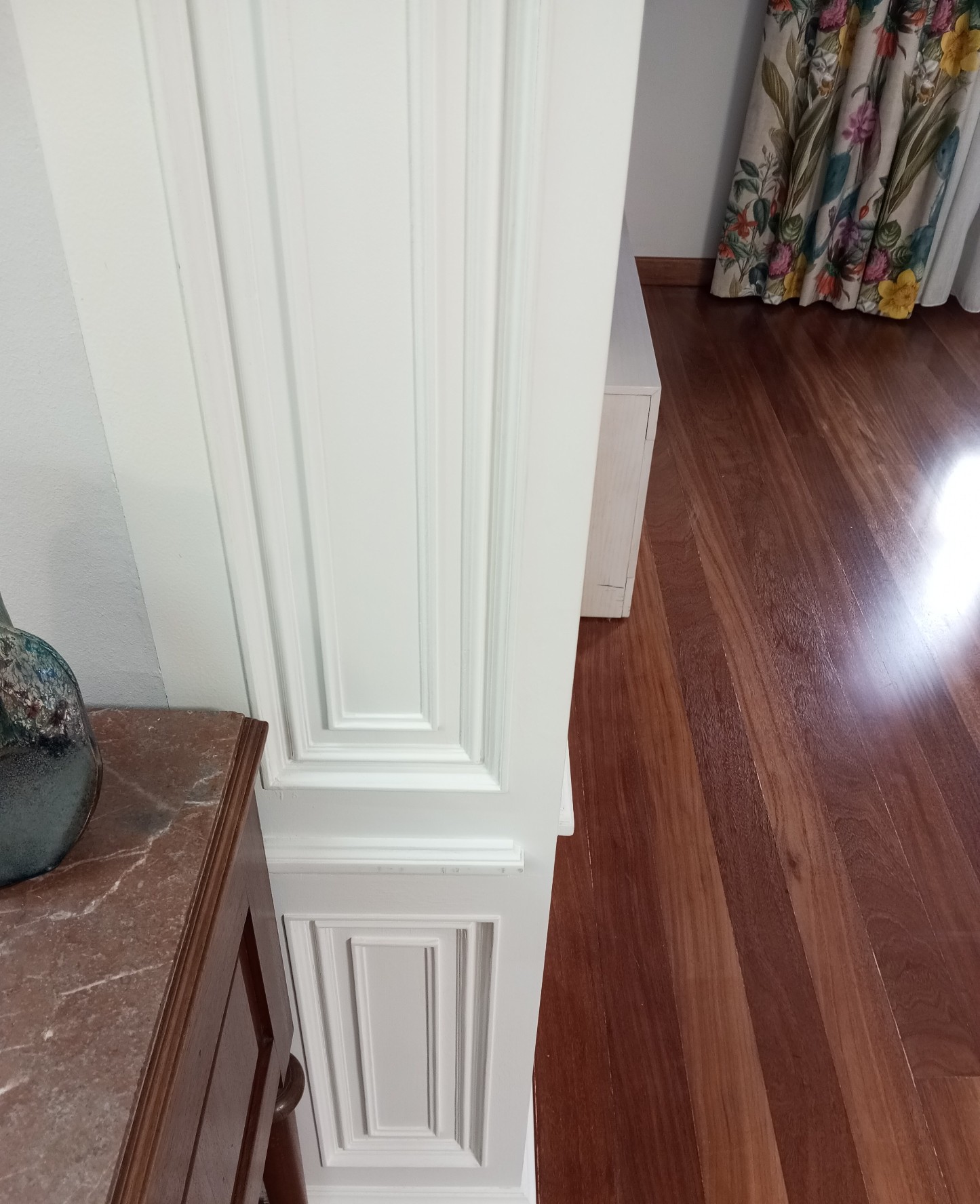 Columna con molduras lacadas en blanco junto a mueble y suelo de madera